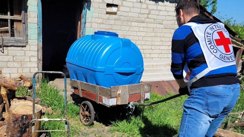 En Röda Korset-volontär drar en blå bevattnings tank på en kärra. Tanken ska installeras för att hjälpa människor som bor i området att vattna sina odlingar.