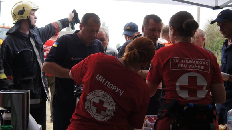 Räddningsarbetare står på en rad och får mat och dryck av Röda Korsets volontärer vid ett tält.