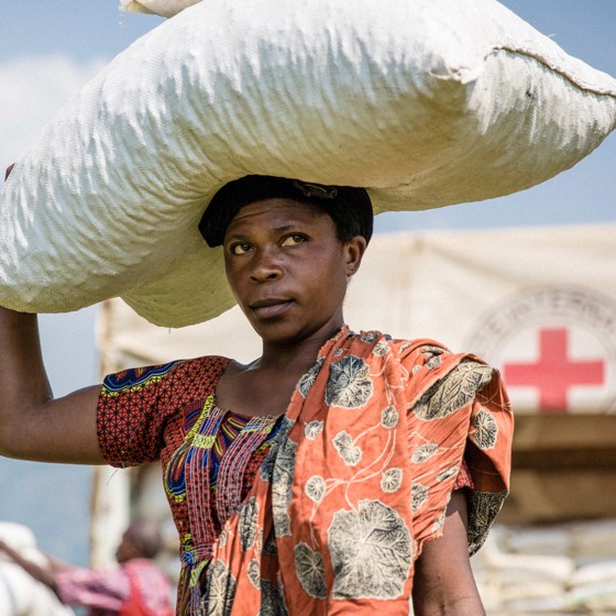 Kvinna bär matpaket på huvudet, Röda Korset i bakgrunden.