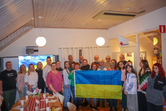 En grupp människor står tillsammans i ett rum. Framför sig håller de Ukrainas flagga i blått och gult.