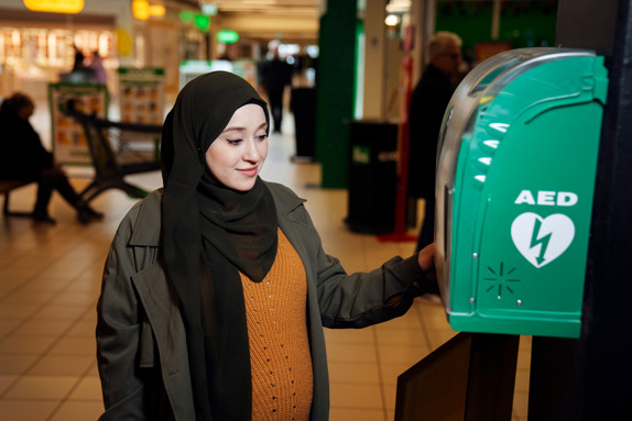 Rewa Almakhwth står vid en utplacerad hjärtstartare i ett köpcentrum.